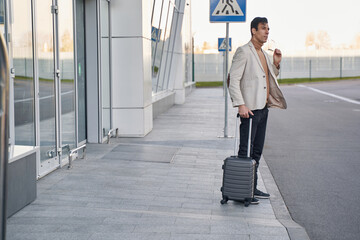 Man taking off glasses while standing outdoors with suitcase