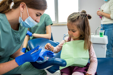  specialist dentist woman brushing the teeth of small child who was brought to the reception. - obrazy, fototapety, plakaty