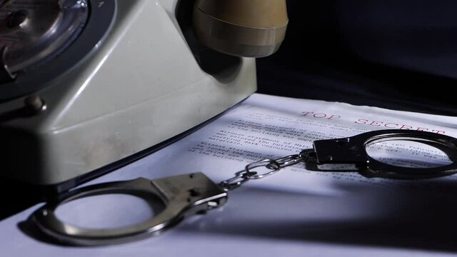 Handcuffs and vintage phone on top secret document in dark room
