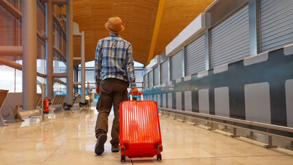 Back view of Young man pulling suitcase in the airport terminal hall which he is casual style...
