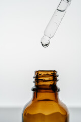 Transparent pipette with cosmetics and bottle on a light background.