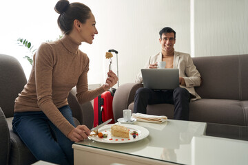 Woman eating cake and looking at man with laptop