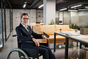Portrait of successful businesswoman using wheelchair and looking at camera smiling while posing in...