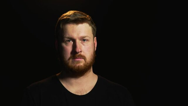 young European man with a red beard stands on a black background and looks into the frame emotion seriousness purposefulness severity