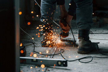 Sparks flying. Close up view of man's legs and hands with slicing tool. Working with metal