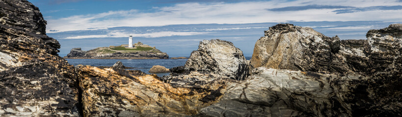 Fototapeta na wymiar Panoramic view of a white lighthouse through a gap in the rocks.