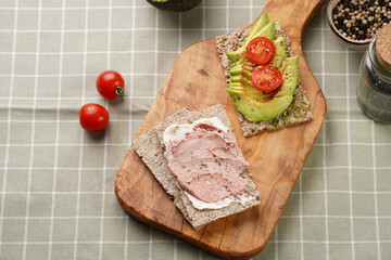 Healthy crunchy crisp bread sandwich with chicken pate, cream cheese, avocado and cherry tomatoes on wooden board