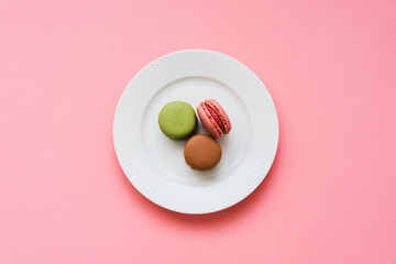 Draufsicht auf französische Macarons auf einem weißen Teller. Rosa Hintergrund, Dessert.