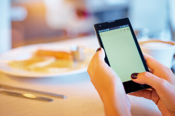 Close up of women's hands holding smartphone with blank copy space screen. Watching video on mobile phone during coffee break.