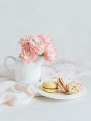 Obraz na płótnie Canvas Two tasty French macarons and a jar with pink carnation flowers on a white background.