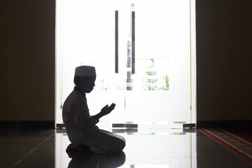 Silhouette side view of boy praying at the mosque 