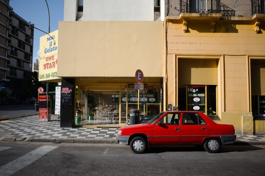 Cordoba, Argentina - January, 2020: Old red Fiat Regata is parked on street corner near restaurant under parking sign. Red car on background of yellow building. Car parking at intersection of streets