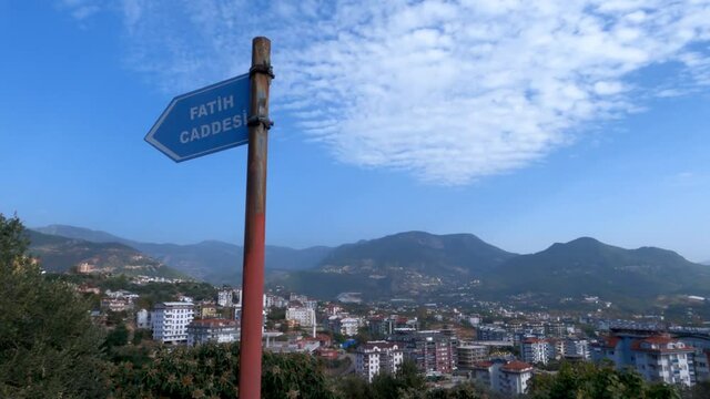 Signpost with Fatih Caddesi written on it in a Turkish city. A small village is in the background. View of blue sky and mountains in Turkey.