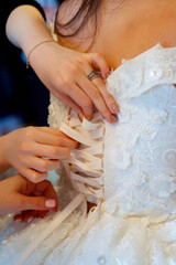 A bridesmaid helps the bride fasten her corset close-up and put on her dress