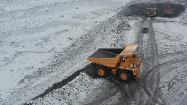 Large quarry dump trucks loaded with coal work at the coal mine in heavy snowfall.