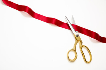 Grand opening, ribbon cut, overhead of gold scissors and red satin satin isolated on white