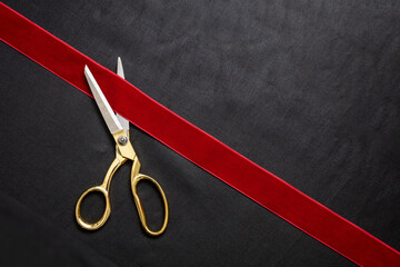 Grand opening, ribbon cut, overhead of gold scissors cutting red velvet ribbon on black