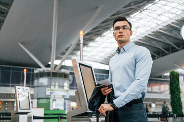 Standing by the terminal. Young businessman in formal clothes is in the airport at daytime