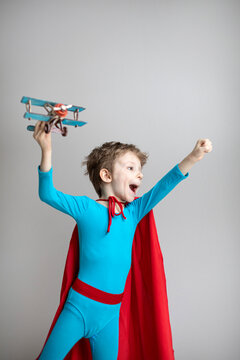 Child in a superhero costume in a red cape is actively playing a model airplane, travel concept.