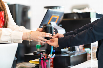 Asian woman barista stands behind the bar and serves coffee to customers In a coffee shop