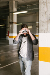 portrait of fashionable cool man on an industrial environment making a photo with a retro camera. vertical shot. High quality photo