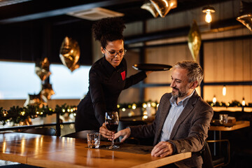 Cheerful caucasian adult man, getting his drink from an african-american waitress.