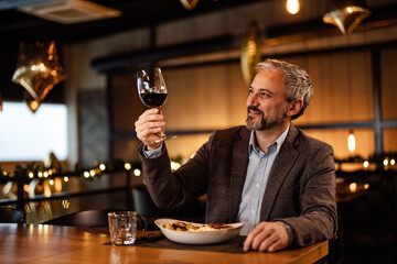 Laughing caucasian adult man, inspecting a glass of wine in his hands, while eating.