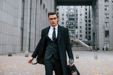 Walking forward. Businessman in black suit and tie is outdoors in the city