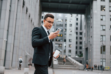 Internet communication by using smartphone. Businessman in black suit and tie is outdoors in the city