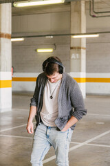 portrait of fashionable cool man on an industrial environment listening to music with earphones an looking down. vertical shot. High quality photo