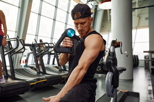 A Young Man Is Using And Enjoying Percussion Massage Gun To Relax And Relief The Pain In Body And Muscles In The Gym