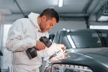 Using special equipment. Man in uniform is working in the auto service