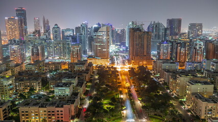 Naklejka premium Skyscrapers in Barsha Heights district and low rise buildings in Greens district aerial night timelapse.