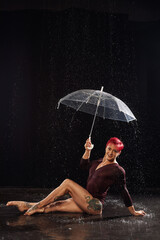 Beautiful young girl in black sportswear with umbrella in aqua studio. Drops of water spread about her fitness body. The perfect figure on the background of water splashes. Classic dark color
