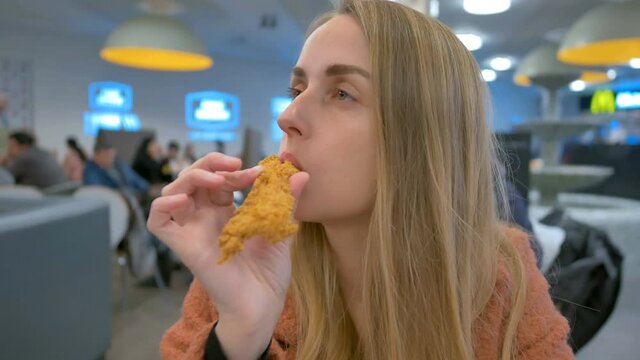 Woman eating chicken by hands on food court in mall