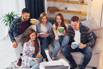 With cups of drink. Group of friends have party indoors together