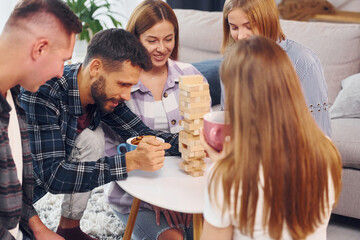 Playing wooden tower game. Group of friends have party indoors together