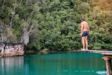 Vacation and activity. Young man enjoying blue tropical lagoon view standing on wooden springboard....