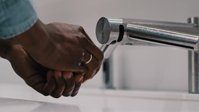 Close-up unrecognizable african american married man guy using washbasin automatic tech in public restroom. Close-up male hands washing with water soap coronavirus protection hygiene skincare concept