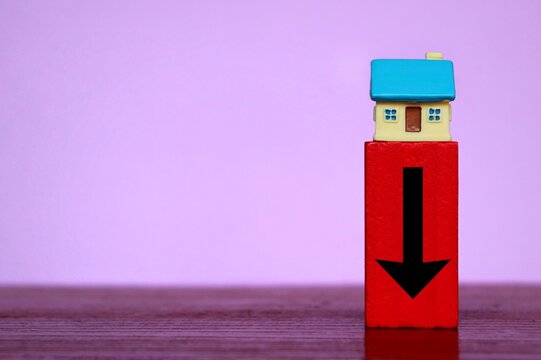Housing market crisis, price drop concept. Miniature house and red wooden cube with downward arrow.