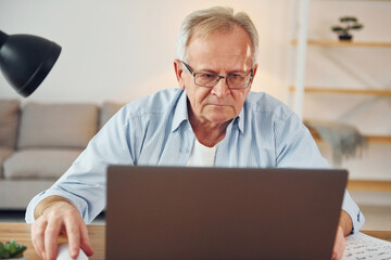 With laptop on table. Senior man in nice clothes is at home