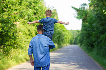 A Happy child with parent on shoulders walk along the road in park background