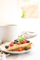 piece of strawberry and blueberry cheescake on plate and cup of tea served for breakfast at home, hotel or cafe. Dessert meal, sweet food