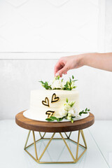 Girl chef decorates wedding cake with flowers. White wedding cake with floral decoration on wooden stand