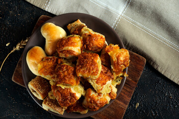 Plate with pies and buns with cheese and sesame seeds on a dark background. Top view, flat lay, selective focus with natural light