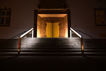 Beleuchtete Tür mit beleuchtetem Geländer einer Treppe in Schweinfurt, Kunsthalle Eingang - obrazy, fototapety, plakaty