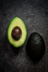 Two halves of fresh avocado on dark stone background .