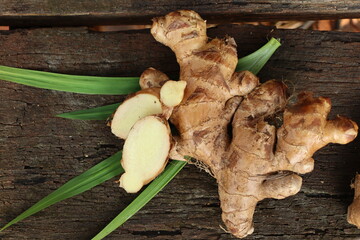 Ginger root and green leaves on wood background