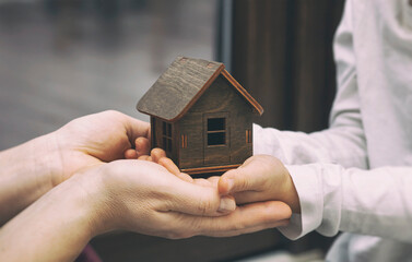 Kid and mother hold the wooden toy house. Adoption concept.