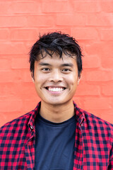 Portrait of handsome young asian man standing outdoors against a red wall background in city and looking at camera - Happy Asian guy portrait - Generation z people concept